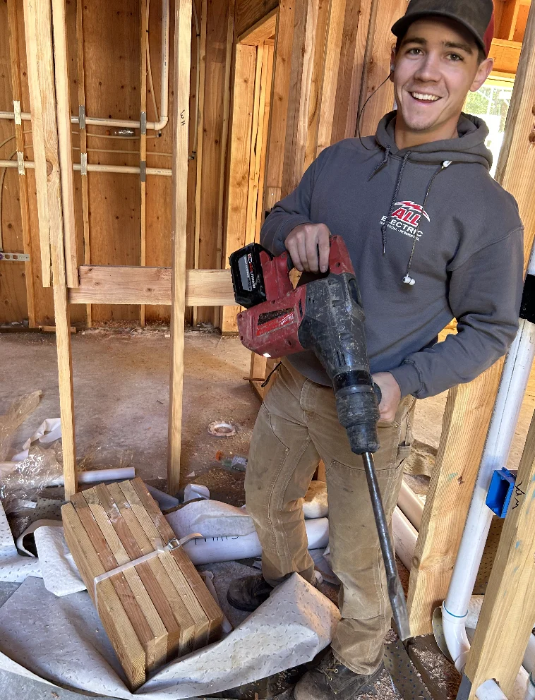 Smiling electrician in a cap holding a drill in a framed house