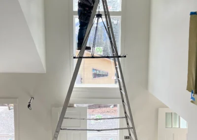 Electrician on a tall ladder installing a chandelier in an entryway